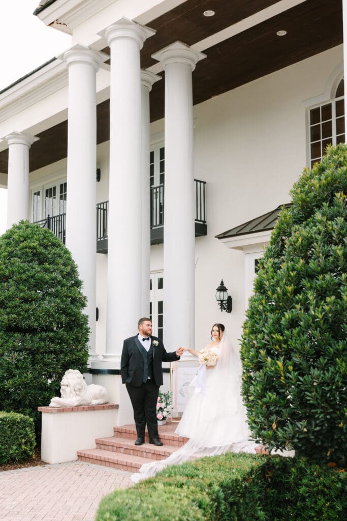 Wedding Photographer in Orlando | Jennifer Holly Light and Airy Wedding Photographer in Orlando | Bride and groom stand on brick steps outside a grand building with white columns. The bride holds a bouquet, and both are smiling, conveying joy.