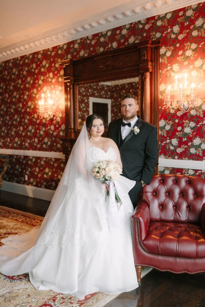 Wedding Photographer in Orlando | Jennifer Holly Light and Airy Wedding Photographer in Orlando | A bride and groom stand in an ornately decorated room with floral wallpaper and a leather couch. The bride wears a white gown and holds a bouquet.