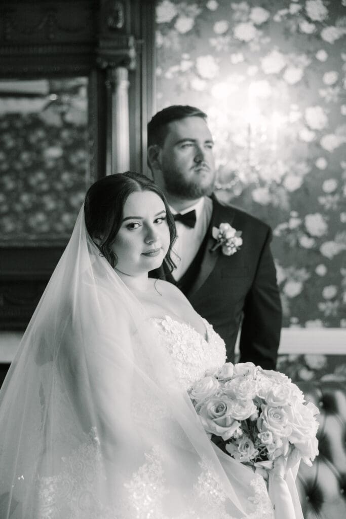 Luxmore Grande Estate | Jennifer Holly Light and Airy Wedding Photographer in Orlando | Bride and groom in elegant attire pose in a vintage setting. The bride holds a bouquet of roses, her expression serene, conveying a timeless romance.