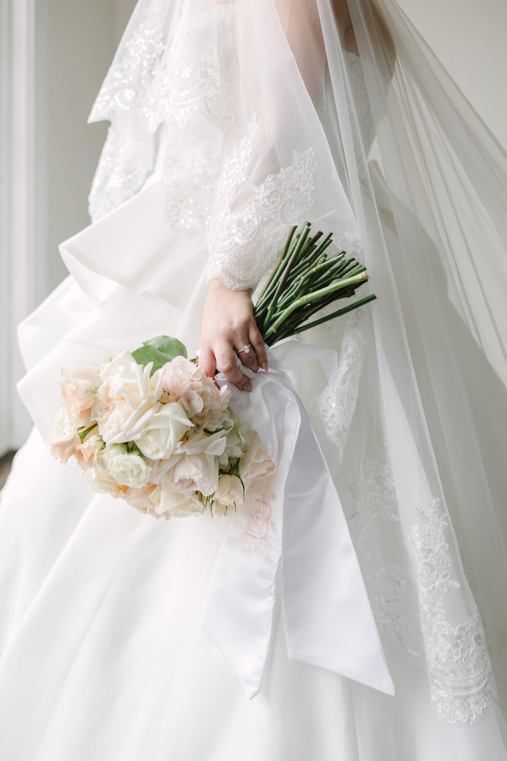 Wedding Photographer Orlando | Jennifer Holly Light and Airy Wedding Photographer in Orlando | A bride in a lace-adorned white wedding gown holds a bouquet of white and blush roses with a long satin ribbon, creating an elegant and romantic tone.
