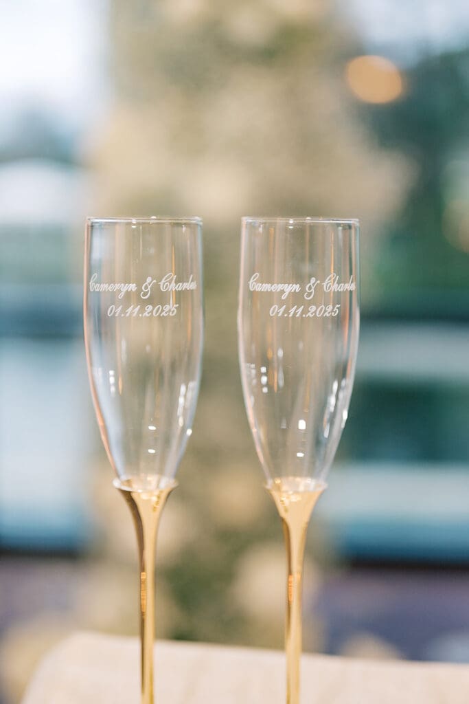 Wedding Photographer Orlando | Jennifer Holly Light and Airy Wedding Photographer in Orlando | Two elegant champagne flutes with gold stems, engraved with names and a date. They are set against a soft, blurred background, suggesting a celebratory event.