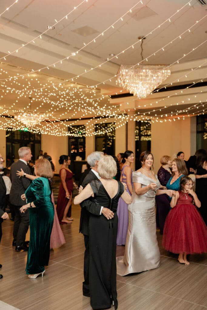 Bella Collina Wedding | Jennifer Holly Light and Airy Wedding Photographer in Orlando | Elegant ballroom scene with guests in formal attire dancing under twinkling string lights and a sparkling chandelier. The atmosphere is joyful and celebratory.