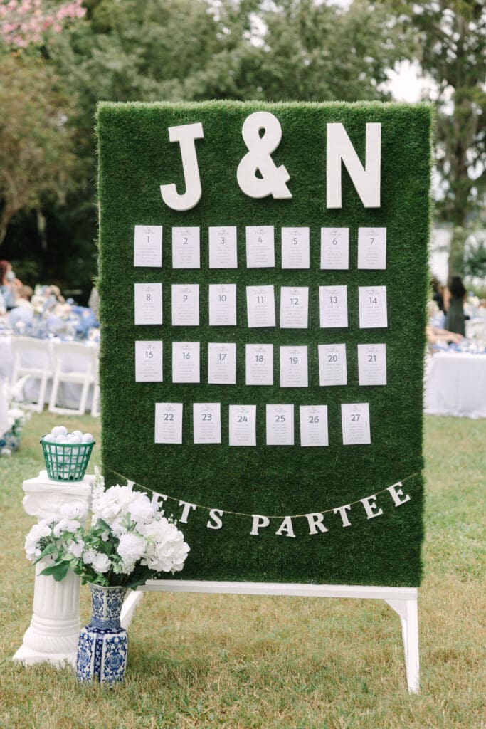 Outdoor Wedding Venues Orlando | Jennifer Holly Light and Airy Wedding Photographer in Orlando | Decorative board with white cards arranged on green turf, labeled "J & N." Below, a banner reads "Let's Parte" with white flowers nearby, in an outdoor setting.