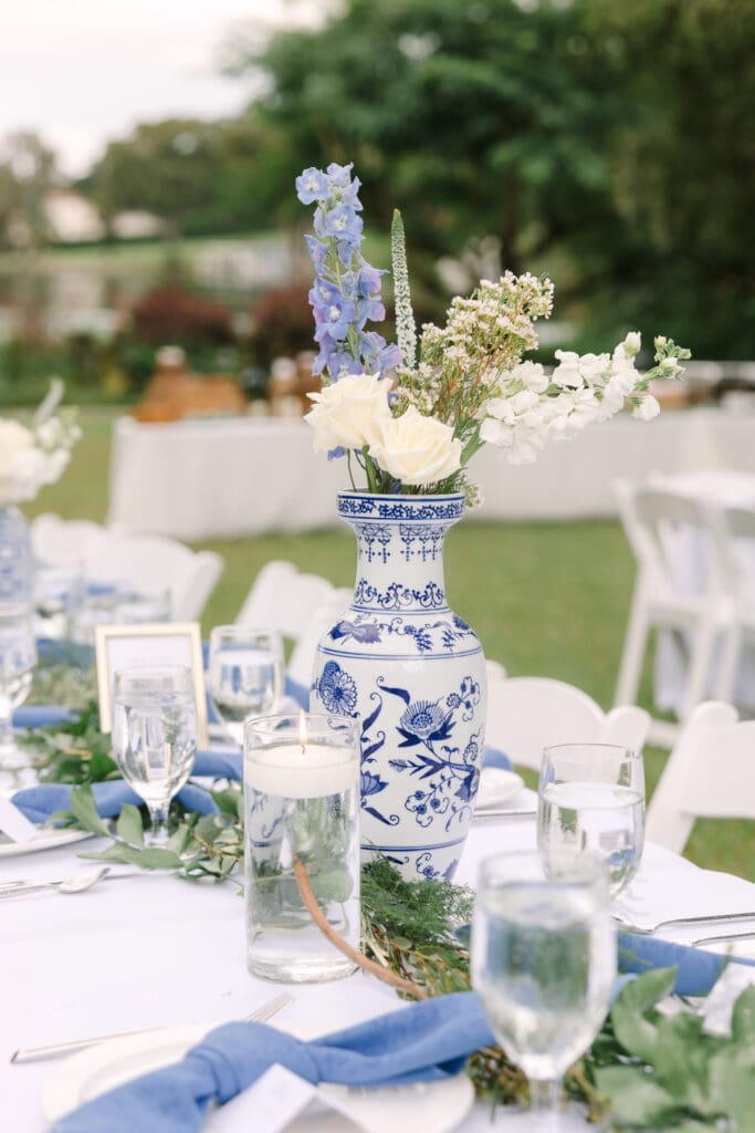 Garden Wedding Venues in Orlando | Jennifer Holly Light and Airy Wedding Photographer in Orlando | Elegant outdoor event table with blue and white floral vase centerpiece, surrounded by white flowers, greenery, blue napkins, and water glasses.