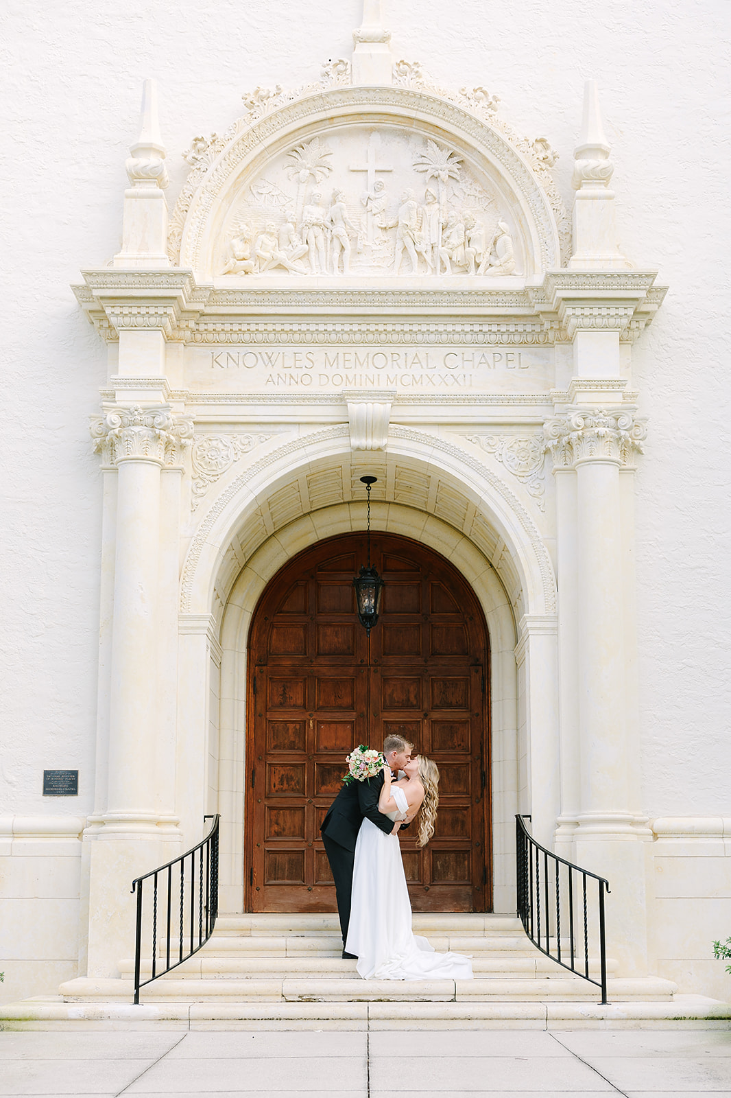 Alfond Inn Winter Park | Jennifer Holly Light and Airy Wedding Photographer in Orlando | A couple shares a romantic kiss in front of the ornate wooden door of Knowles Memorial Chapel. The bride holds a bouquet, and the atmosphere is joyful and serene.