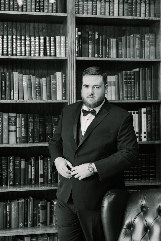 Wedding Venues in Central Florida | Jennifer Holly Light and Airy Wedding Photographer in Orlando | A man in a tuxedo stands confidently in front of a bookshelf filled with books. The setting is formal, conveying elegance and sophistication.