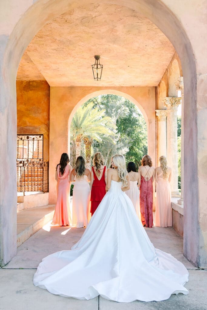 bride in white with bridesmaids in colors of the sunset under stone archways at The Howey Mansion captured by Jennifer Holly Photography
