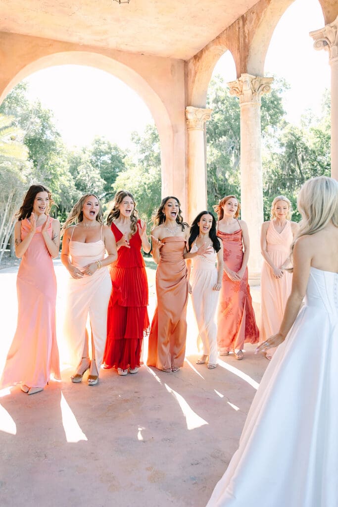 bride in white with bridesmaids in colors of the sunset under stone archways at The Howey Mansion captured by Jennifer Holly Photography