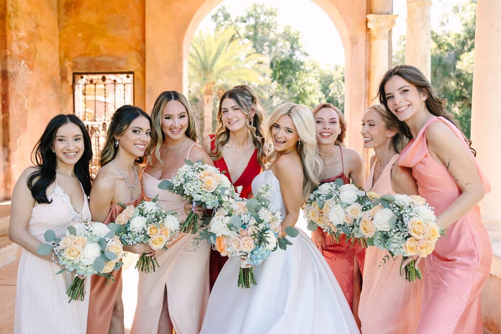 bride in white with bridesmaids in colors of the sunset under stone archways at The Howey Mansion captured by Jennifer Holly Photography