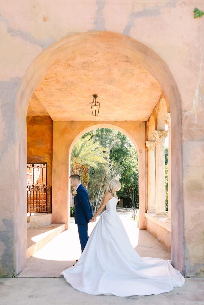 bride and groom first touch under stone archway holding bouquet at The Howey Mansion captured by Jennifer Holly Photography