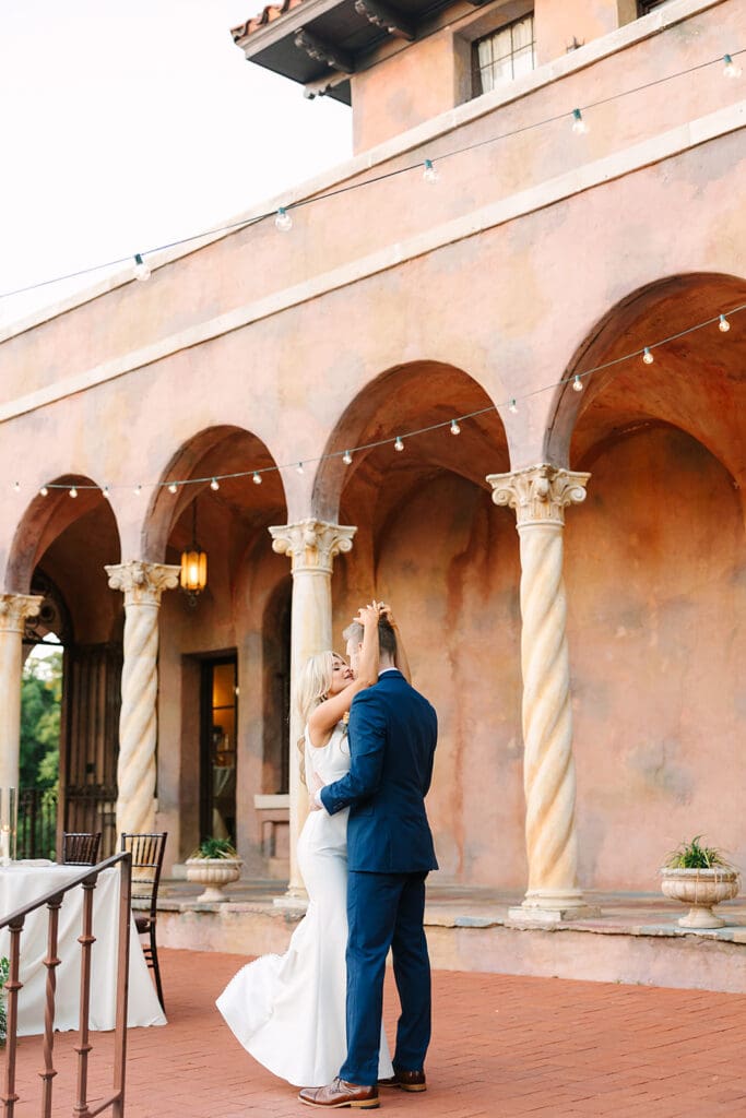 A couple in formal attire dances on a brick patio at Howey Mansion, a Florida estate wedding venue, with arched columns and string lights—captured by Jennifer Holly Photography.
