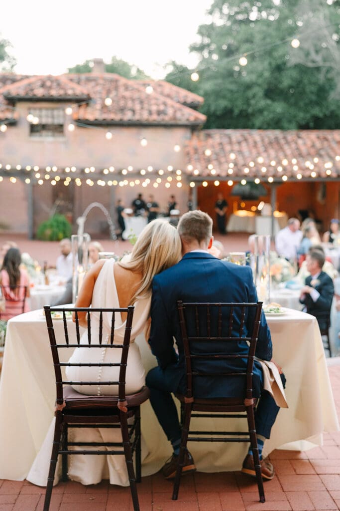 bride and groom sit at their sweetheart table overlooking their outdoor wedding reception at The Howey Mansion captured by Jennifer Holly Photography
