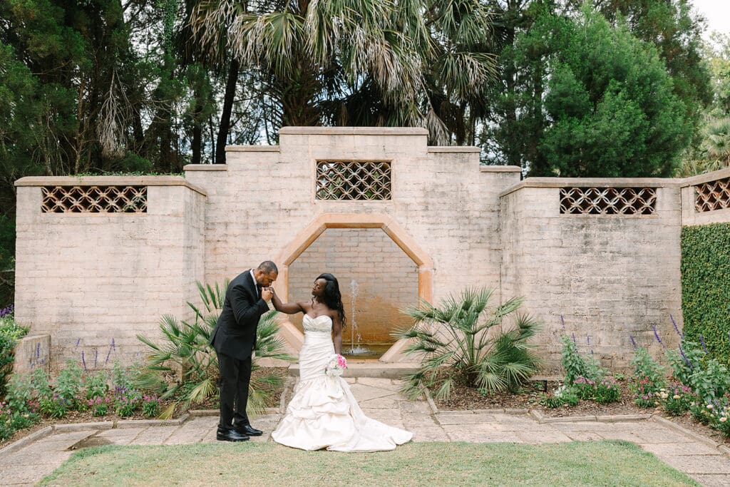 bride and groom stand in front of a stone wall and fountain at Bok Tower Gardens in an elopement portrait captured by Jennifer Holly Photography, an Orlando elopement and wedding photographer