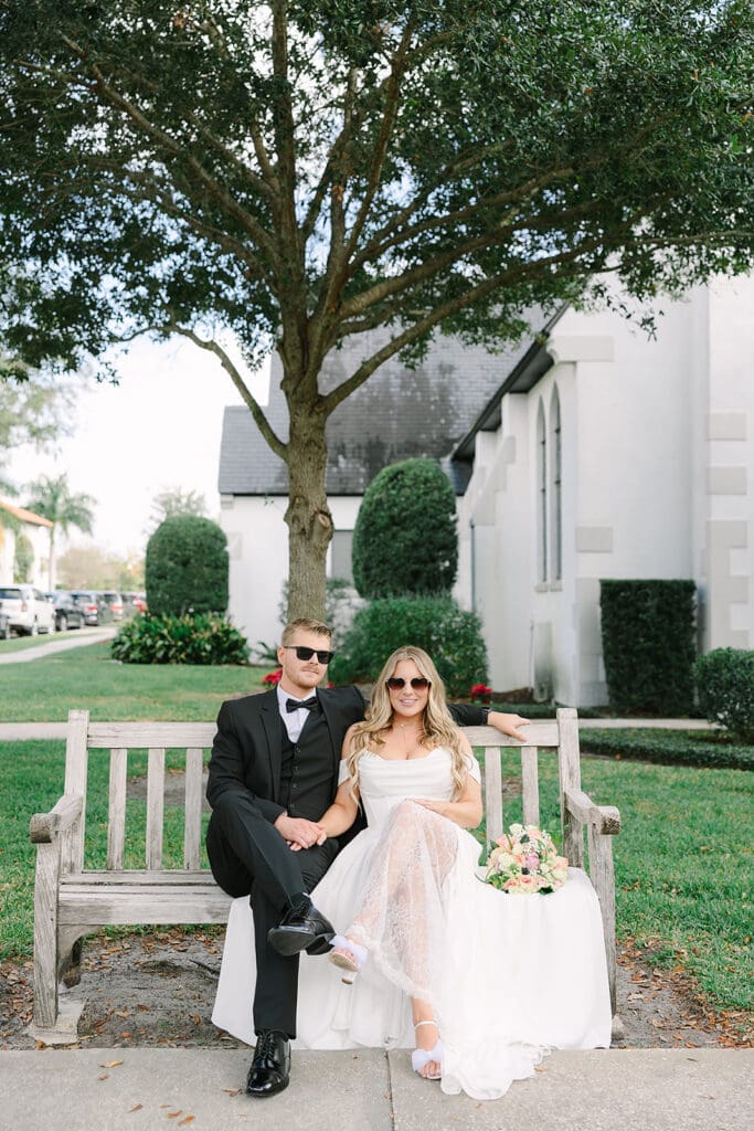 bride and groom sitting on a bench wearing sunglasses at Rollins College in an elopement portrait captured by Jennifer Holly Photography, an Orlando elopement and wedding photographer