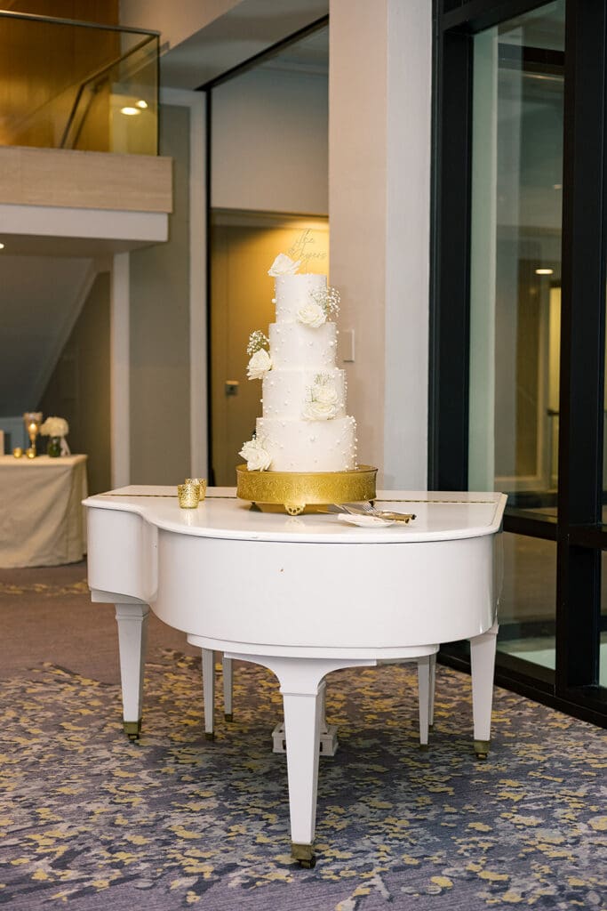 four-tiered white wedding cake on a grand piano at a wedding reception at Hyatt Regency Grand Cypress Resort in Orlando, Florida, captured by Jennifer Holly Photography