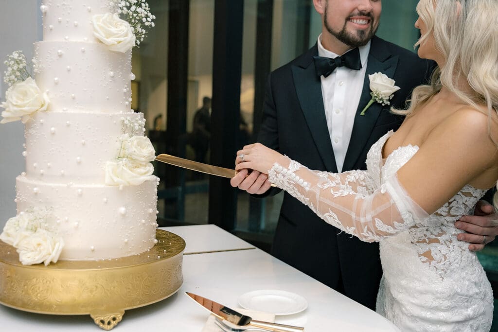 bride and groom cutting a four-tiered white wedding cake on a grand piano at a wedding reception at Hyatt Regency Grand Cypress Resort in Orlando, Florida, captured by Jennifer Holly Photography