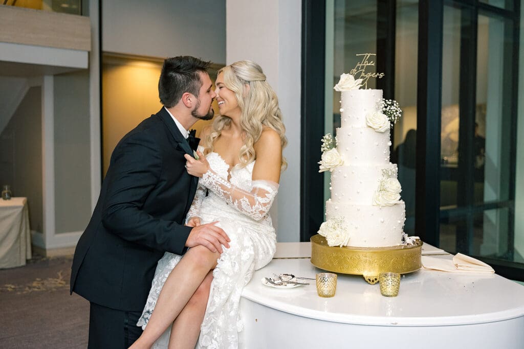bride and groom with a four-tiered white wedding cake on a grand piano at a wedding reception at Hyatt Regency Grand Cypress Resort in Orlando, Florida, captured by Jennifer Holly Photography